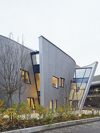 Außenansicht des Maggie Center in London. Man sieht ein geschwungenes Gebäude aus Holz.