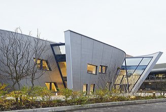Exterior view of the Maggie Center in London. You can see a curved wooden building.