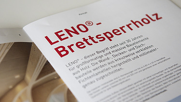 Foto der Innenseite der Broschüre Holzbauelemente von ZÜBLIN Timber. Man sieht links LENO als Gewölbebalken und rechts die Überschrift LENO-Brettsperholz mit Text.