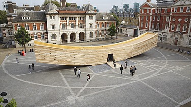 Foto vom Marktplatz und von der geschwungenen Holzskulptur The Smile in London. Der Holzkasten ist begehbar und soll einen lachenden Mund darstellen.