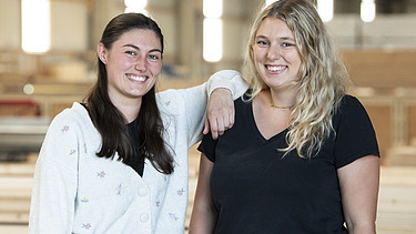 Foto von zwei jungen Frauen, die in die Kamera lächeln.