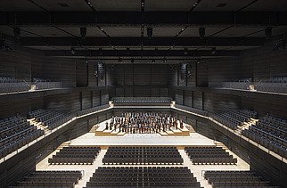 Foto der Interimsspielstätte Gasteig in München. Zu sehen ist der bestuhlte Bühnenraum mit Orchester.