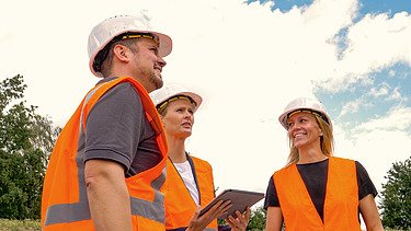 Photo of three people in construction site clothing talking to each other.