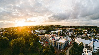 Foto der Uni Witten von außen. Man sieht den Rohbau aus Holz in der Vogelperspektive in dämmriger Lichtstimmung.